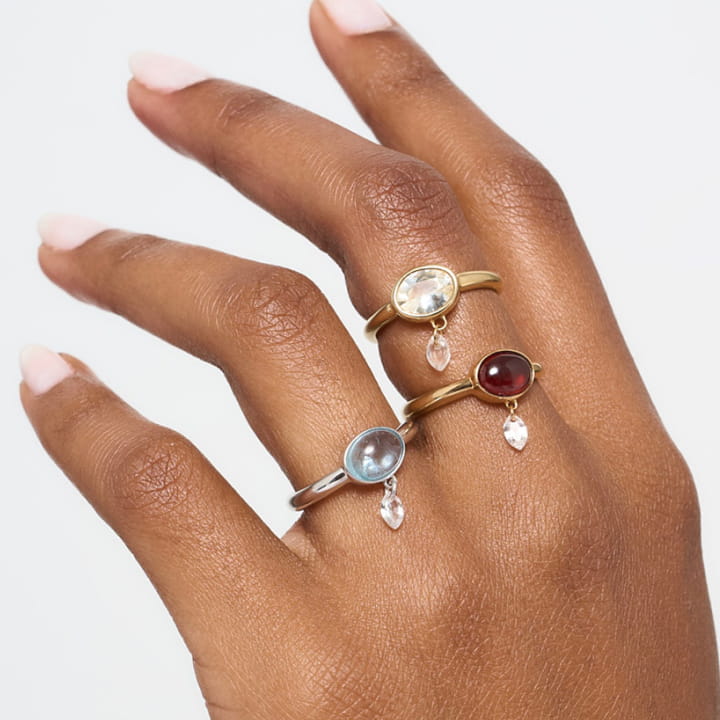 Juicy Rings in garnet, white sapphire, and aquamarine, on a hand.